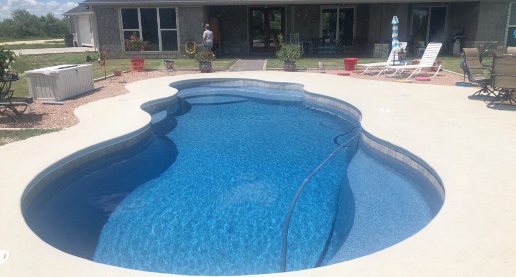 Freeform swimming pool with blue tile lining and a cleaning hose