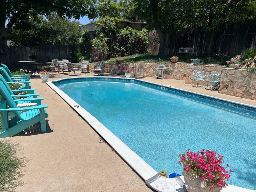 Rectangular blue swimming pool beside turquoise chairs and a stone retaining wall.