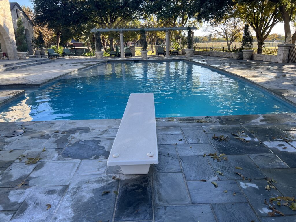 Rectangular outdoor pool with a diving board, stone deck, and pergola