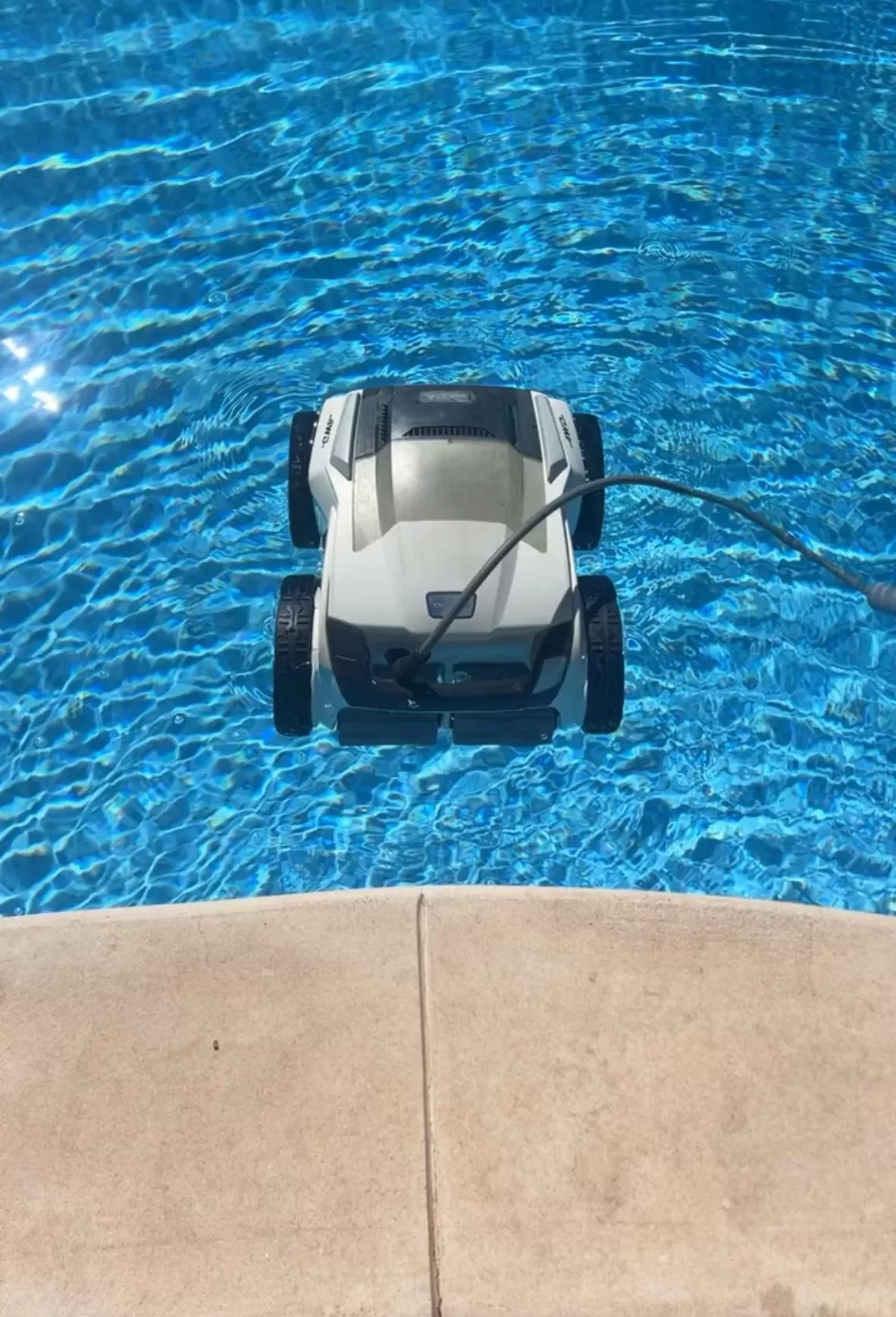 Gray corded robotic pool cleaner on a submerged pool step in blue water