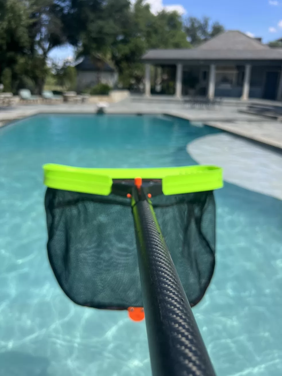 Green-rimmed leaf net on a telescopic pole held over a swimming pool.